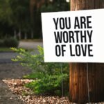 A positive message sign "You are worthy of love" in a park setting.