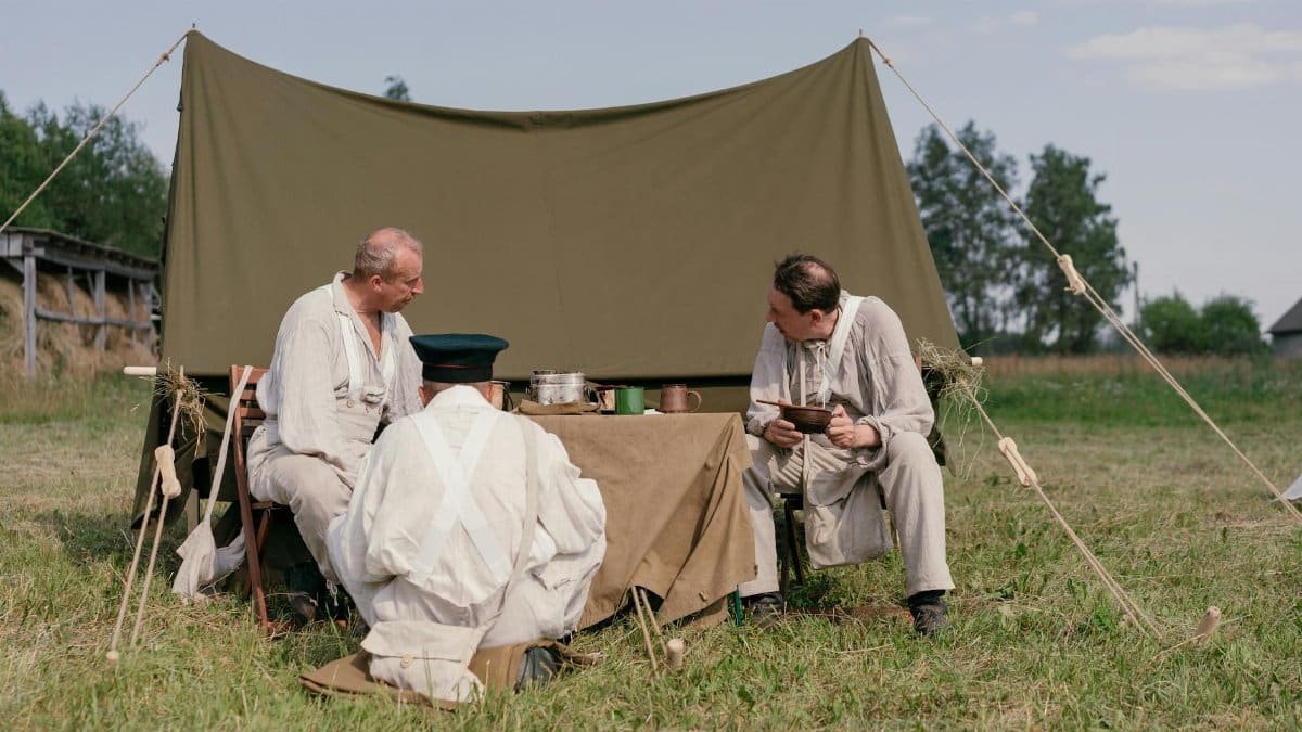 Men in historical costumes depicting a past era, gathered around a tent outdoors.