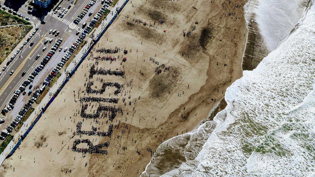A large group on a beach forms the word "Resist" in powerful demonstration.