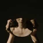 Artistic portrait of a woman holding a mirror, reflecting her face, with a dark, moody background.