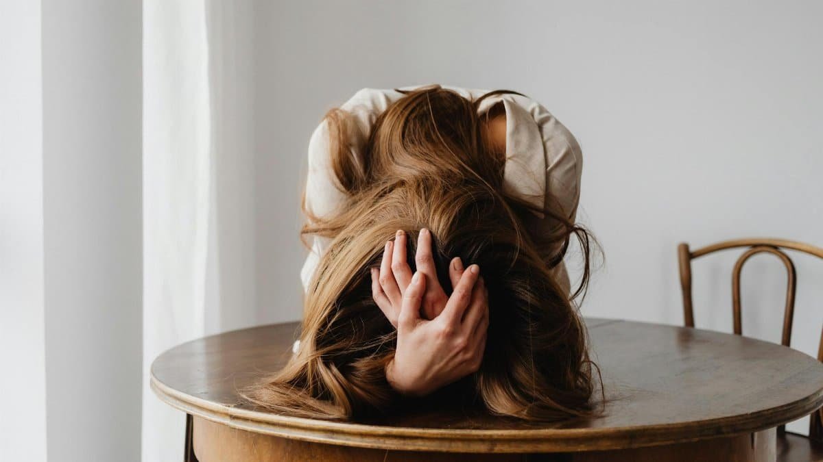 A woman showing despair with her head down on a table, indicating stress.