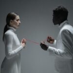 A conceptual studio shoot of an interracial couple connected by a red thread, symbolizing connection.