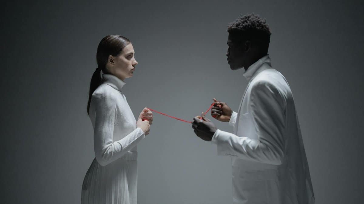 A conceptual studio shoot of an interracial couple connected by a red thread, symbolizing connection.