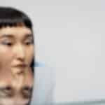 A woman gazes thoughtfully at a blue ball with reflections on a glass surface.