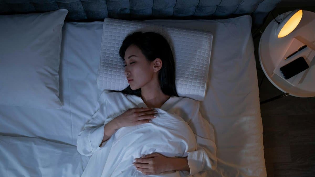 Calm and peaceful woman resting in bed under dim lighting, promoting relaxation.