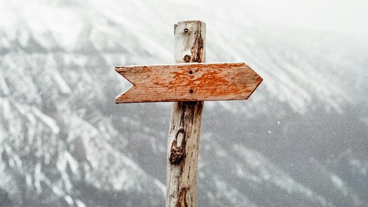A wooden arrow signpost points the way amidst a snowy mountain landscape.