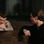 A tattooed man in conversation with a priest inside a church, sharing a moment of confession.