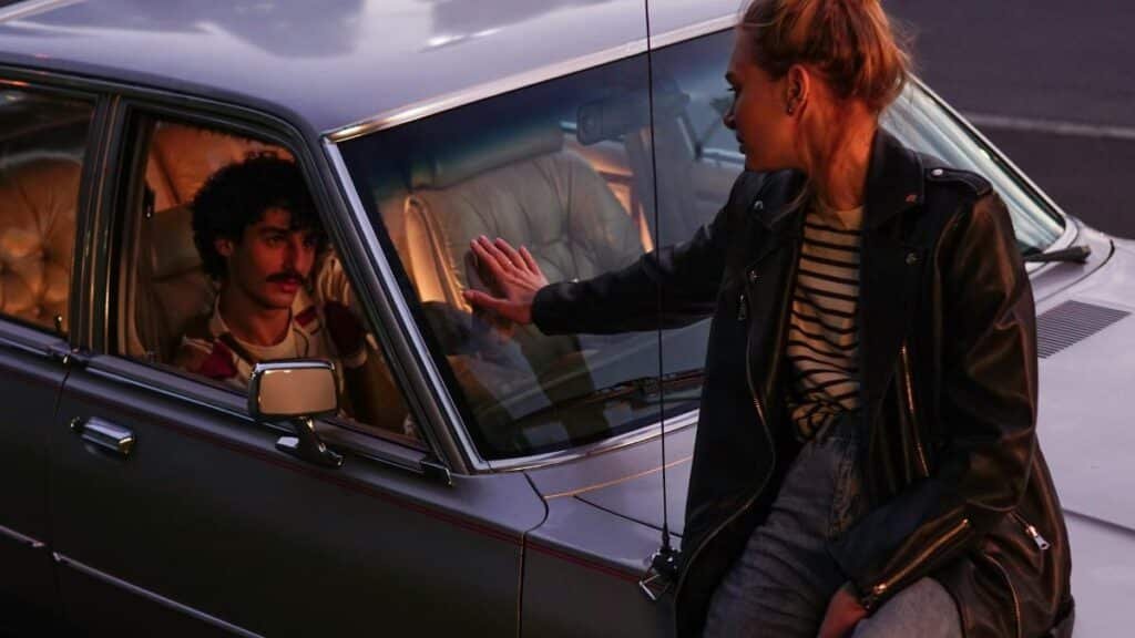 A dramatic moment between a couple by a classic car at dusk.