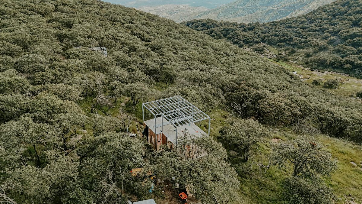 Aerial view of a construction site in a dense forest on a mountainside, showcasing industrial progress and nature.