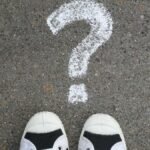 Sneakers on pavement with a chalk question mark, symbolizing curiosity or decisions.