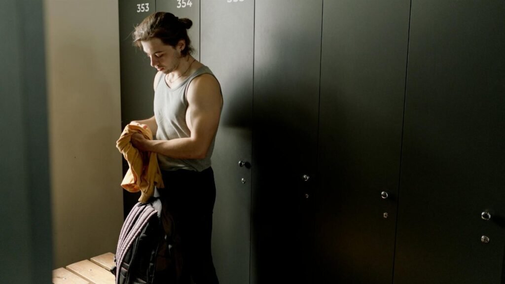 A fit young man with a duffel bag in a locker room, ready for a workout session.