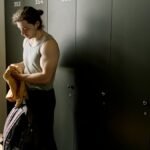 A fit young man with a duffel bag in a locker room, ready for a workout session.