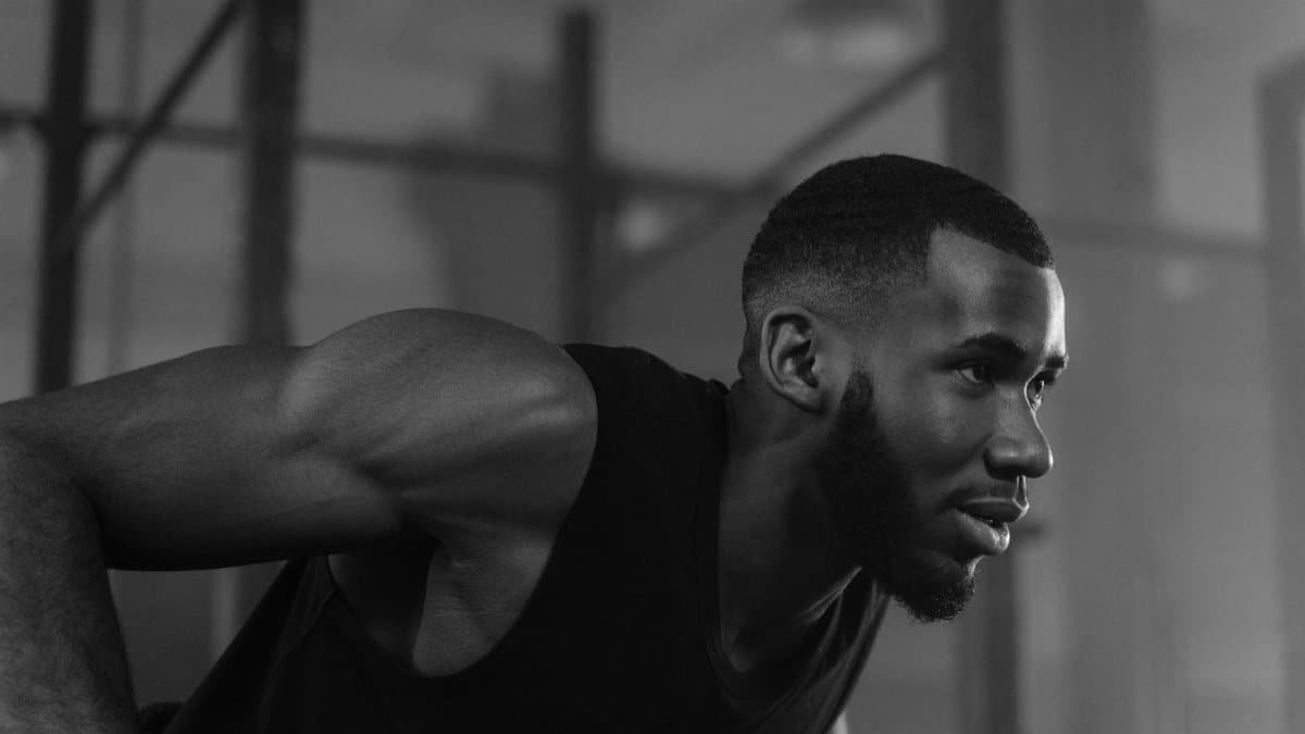 Black and white image of an African American athlete deeply focused during an indoor workout with a determined expression.