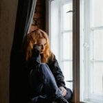 A woman sits by a window, lost in deep thoughts and moody light.