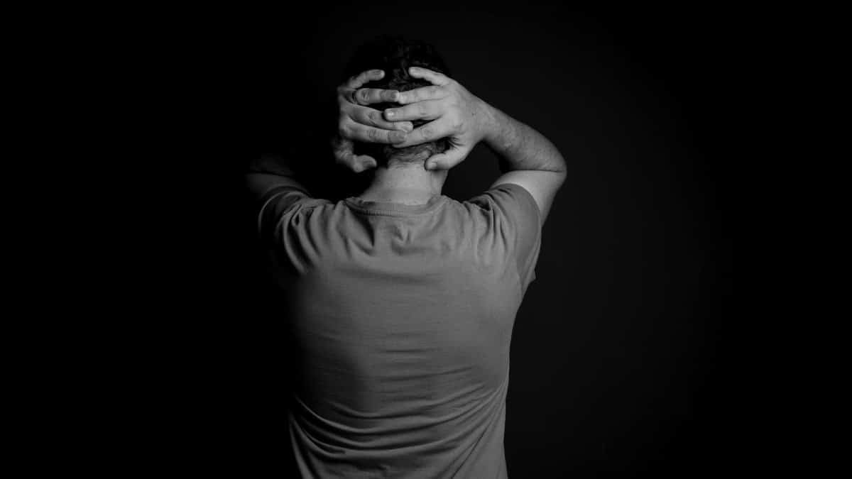 Black and white portrait of a man with hands on head, conveying stress and frustration.