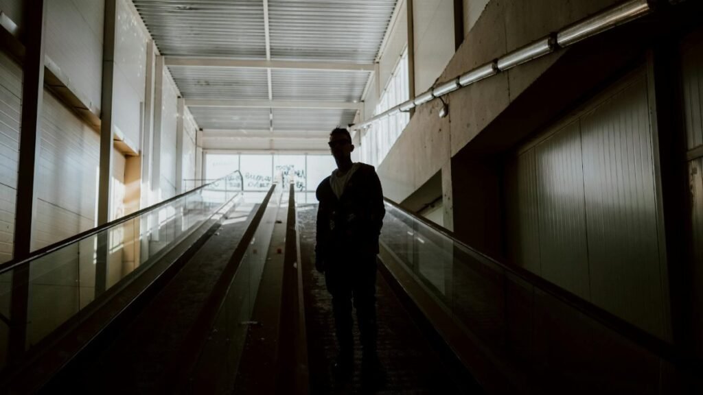 A silhouette of a person standing on an indoor escalator in a modern building.