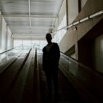 A silhouette of a person standing on an indoor escalator in a modern building.