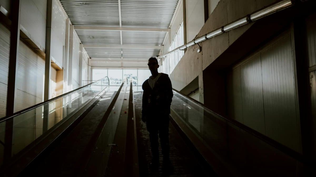 A silhouette of a person standing on an indoor escalator in a modern building.