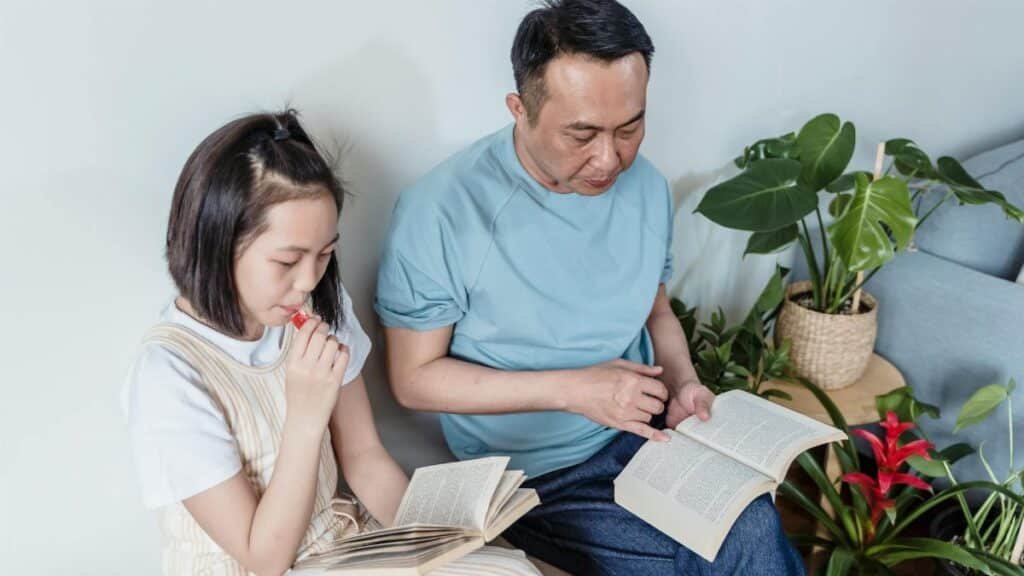 Father and daughter enjoying a quiet reading session indoors surrounded by plants.