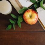 Aesthetic study environment with an apple, candle, and open textbooks on a wooden table.