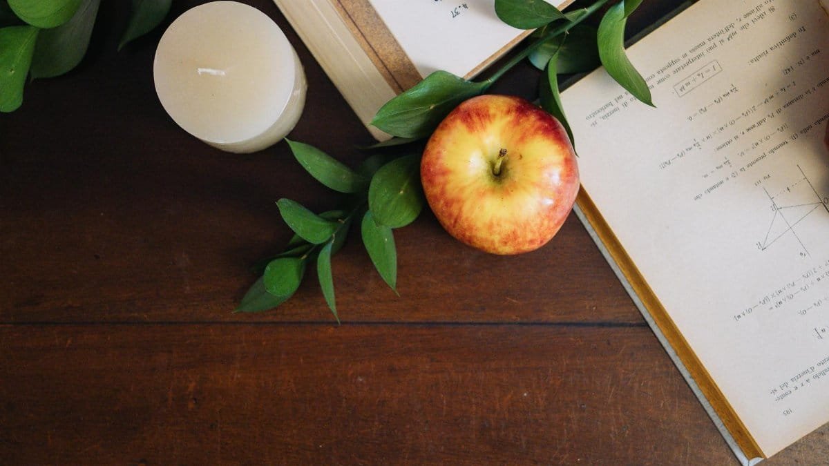 Aesthetic study environment with an apple, candle, and open textbooks on a wooden table.