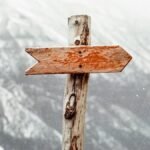 A wooden arrow signpost points the way amidst a snowy mountain landscape.