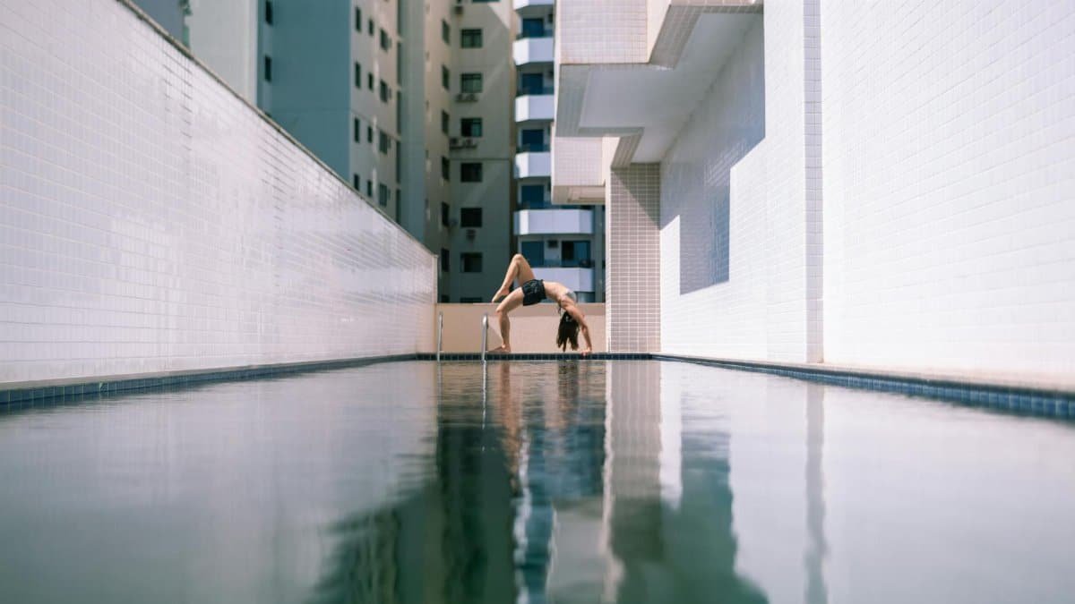 A woman practicing yoga poses by an urban pool, demonstrating flexibility and modern lifestyle.