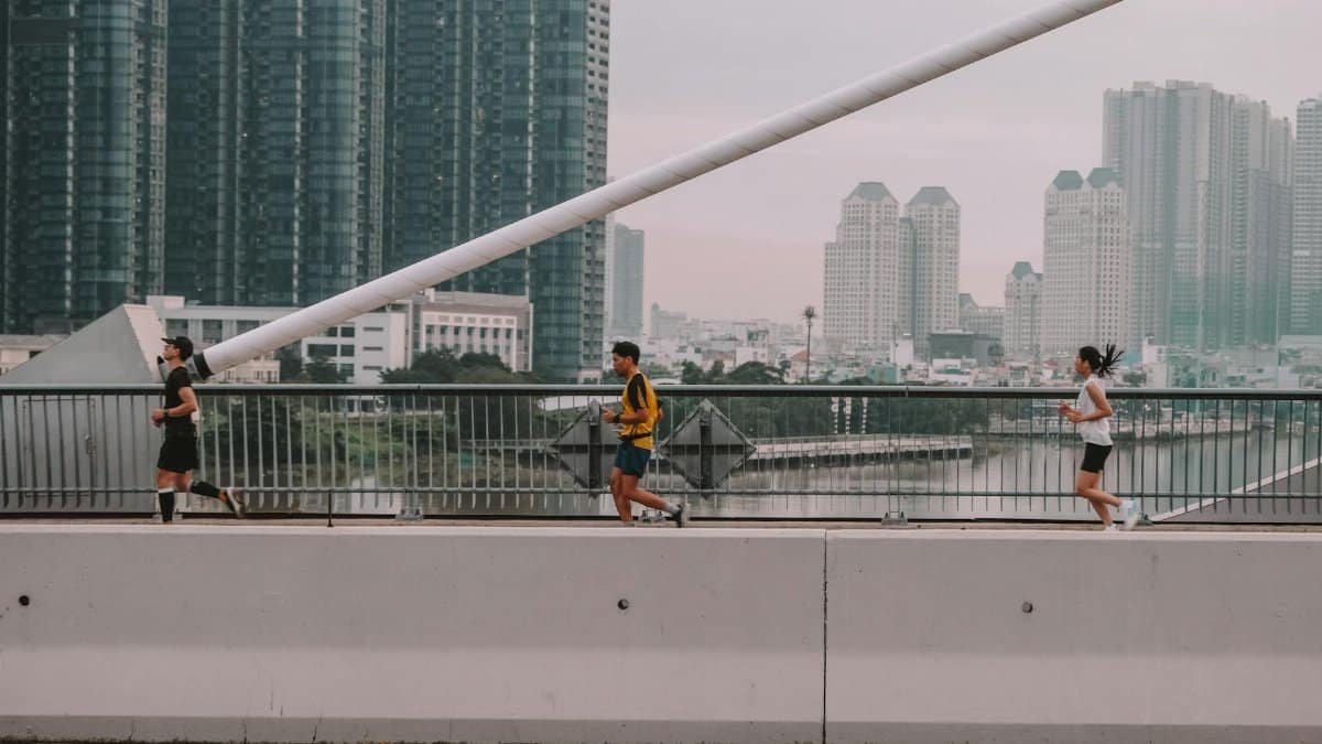 Three people jogging on a bridge with a city skyline backdrop, showcasing an active urban lifestyle.