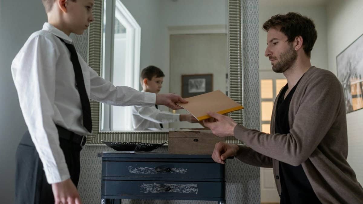 A father and son exchanging an envelope in an indoor setting, reflecting parenthood and communication.