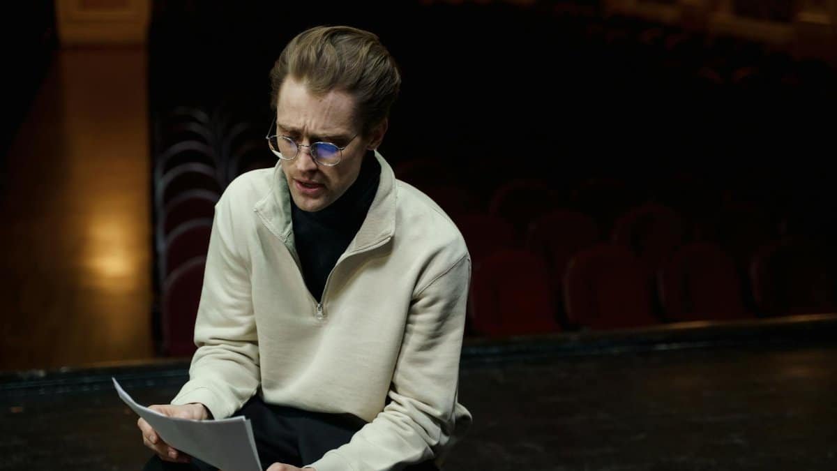 An actor rehearses lines on a theater stage, conveying focus and dedication in a dimly lit setting.