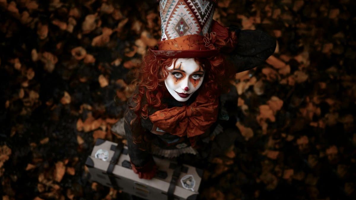 A woman in a vibrant costume and painted face poses on fallen leaves, capturing the essence of fall and Halloween.