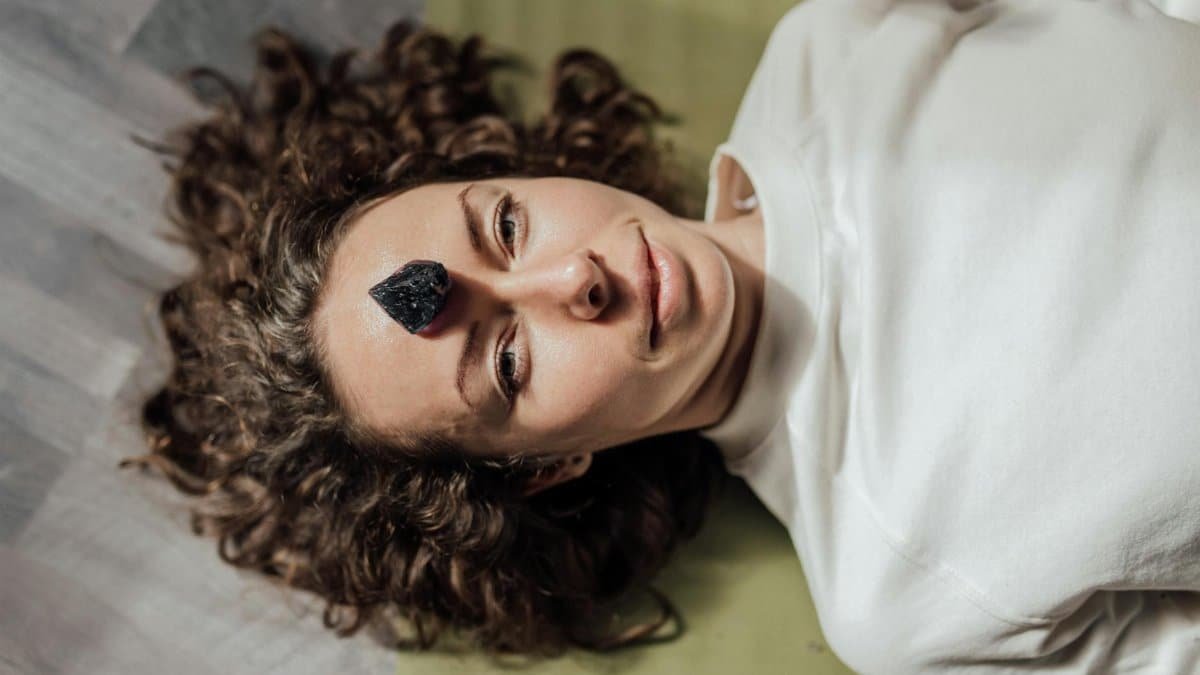 Young woman lying down with a healing crystal on her forehead, promoting relaxation and meditation.