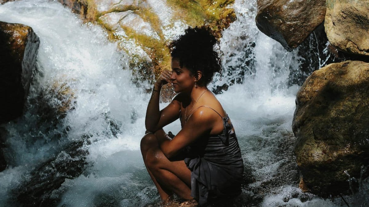 A serene moment of a woman sitting by a rushing waterfall surrounded by rocks.