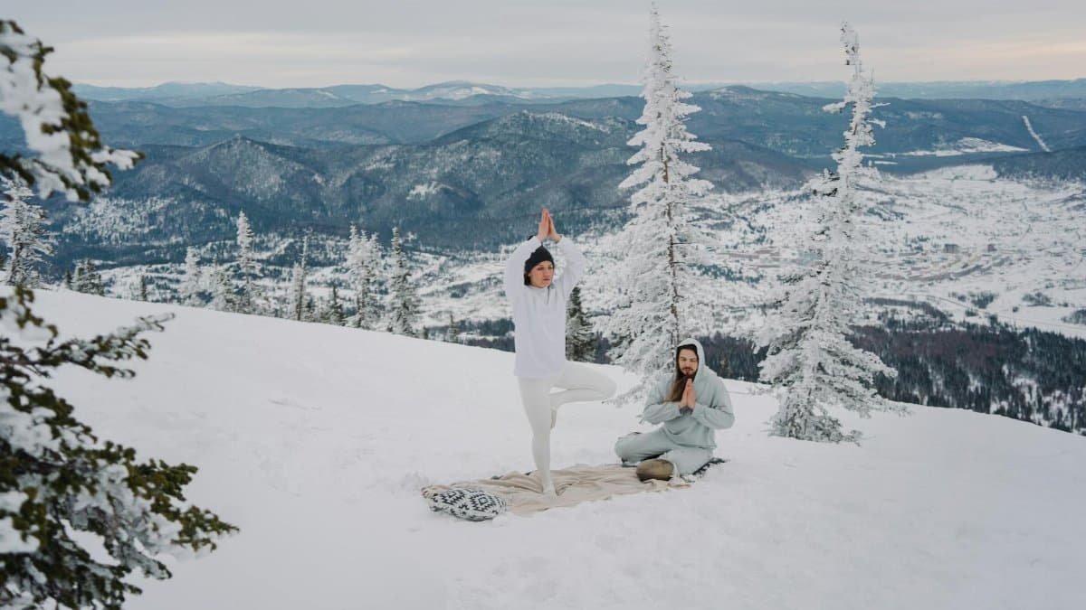 Couple practicing yoga and meditation in a snow-covered mountain landscape, embracing winter serenity.