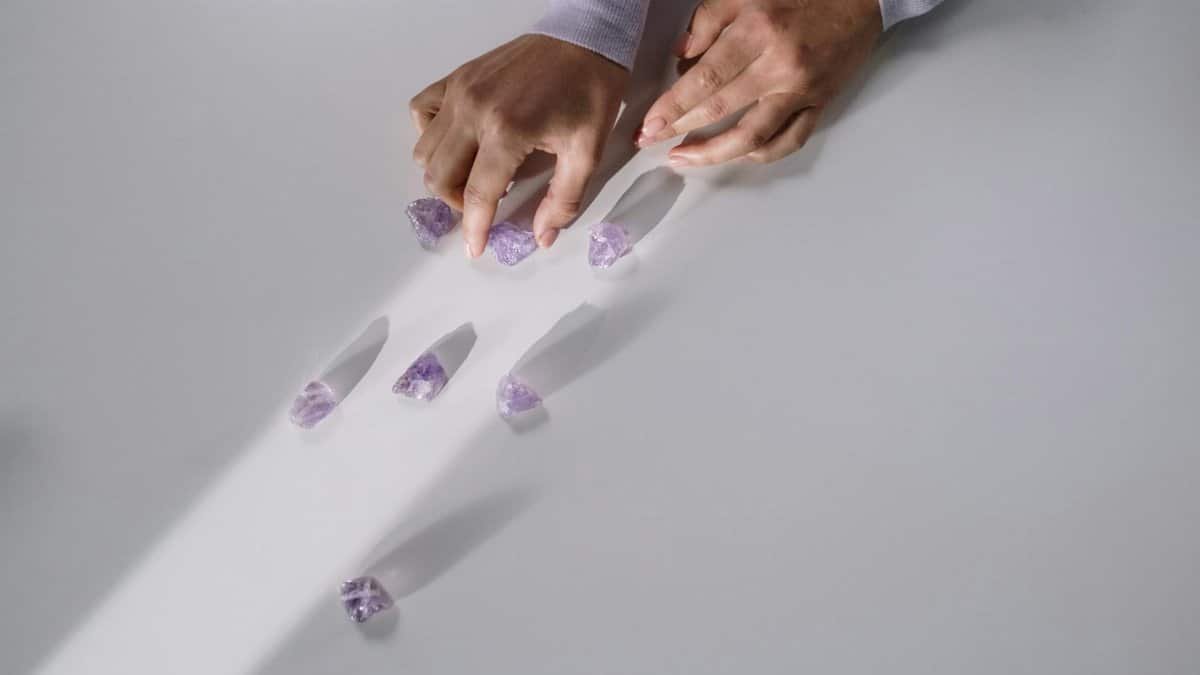 Hands arranging amethyst crystals on a white surface, creating patterns with light and shadows.