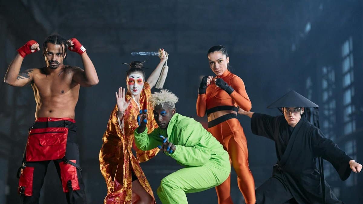 Five diverse individuals in cosplay pose as martial arts characters in an industrial setting.