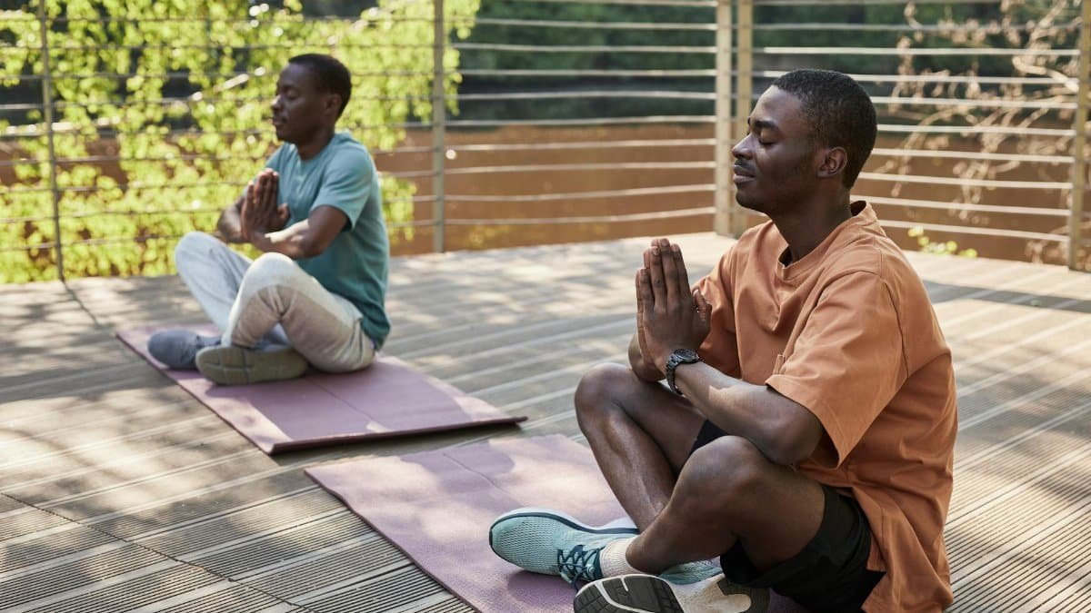 Two men meditating outdoors on yoga mats in a serene setting.