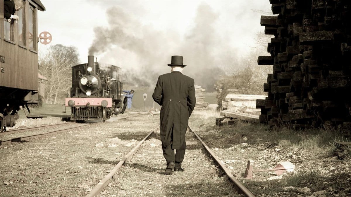 Retro scene of a man in a suit walking along a railroad with a steam train.