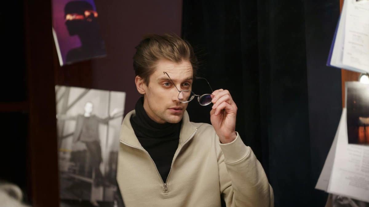 Actor preparing for a role backstage in a dressing room, adjusting glasses and looking at the mirror.