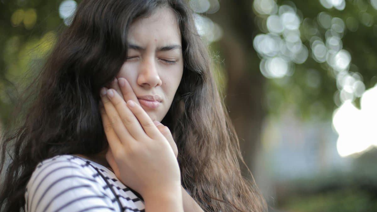 Portrait of a young woman feeling toothache, showing discomfort outdoors with a pained facial expression.