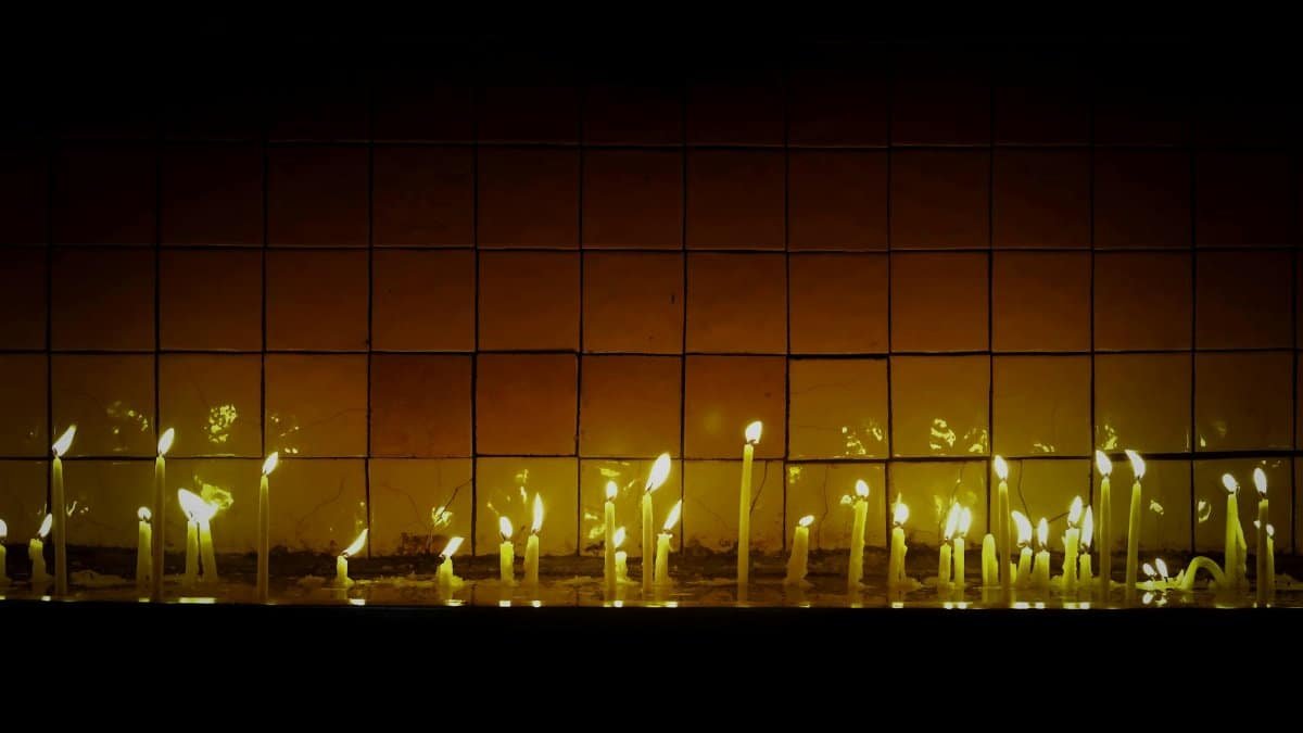 A row of candles casting warm reflections on a tiled wall, creating a serene and contemplative atmosphere.