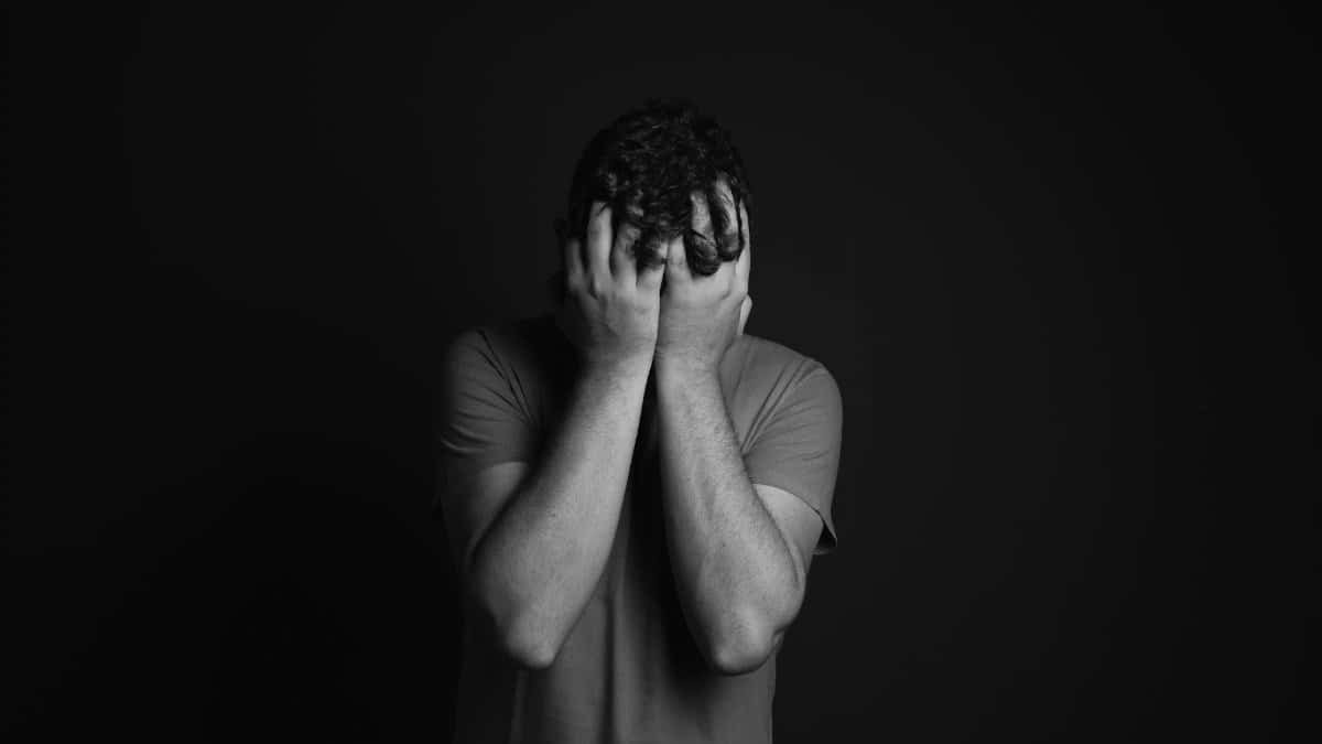 A grayscale portrait of a man covering his face, depicting emotion and mental health themes.