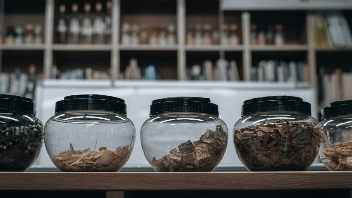 Glass jars with dried herbs and roots on a shelf in a traditional Korean pharmacy.