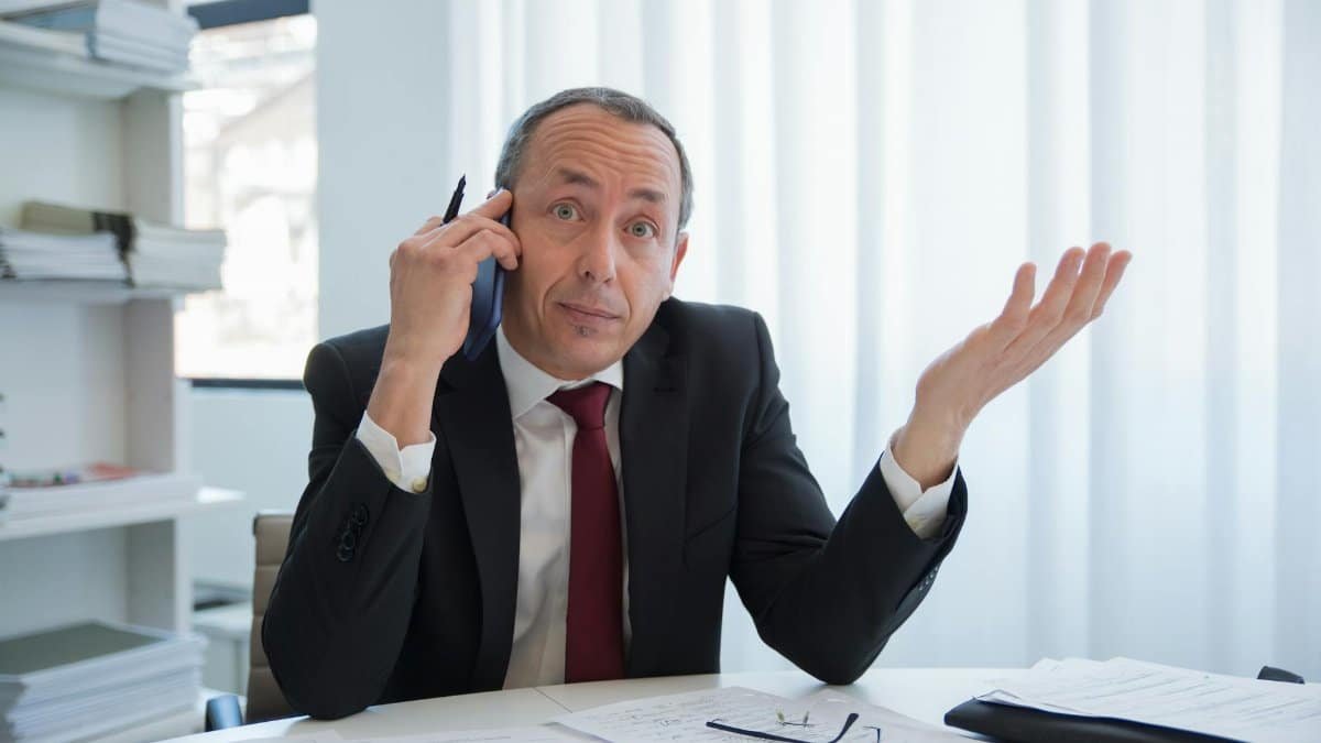 Business professional in a suit talks on the phone while gesturing in an office.