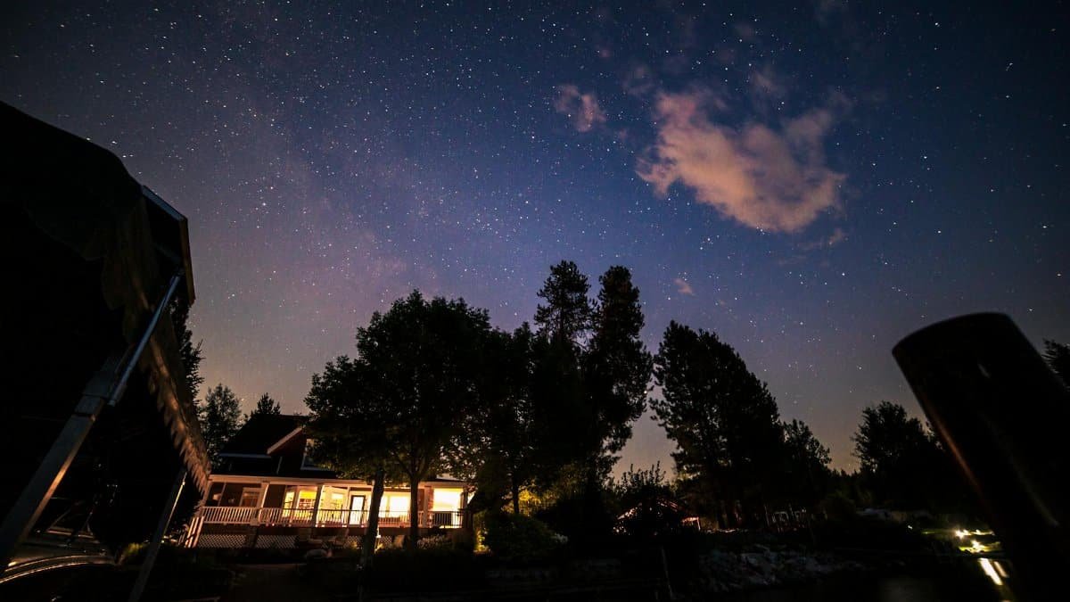 A tranquil view of a star-filled night sky over a lakeside house, capturing nature's beauty.