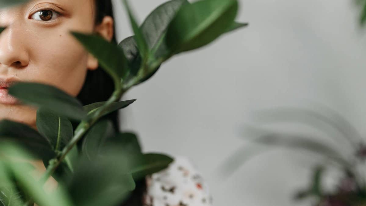 Close-up portrait of a woman partially hidden behind vibrant green leaves.