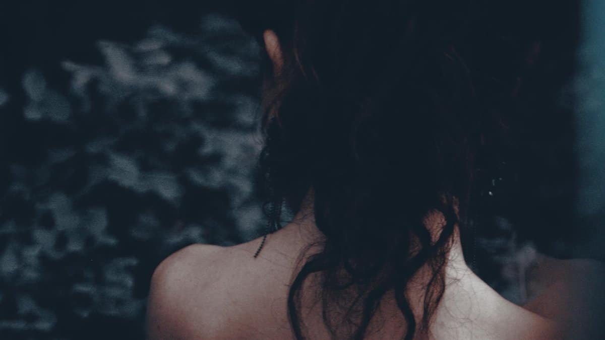 Artistic portrait of a woman seen from behind, highlighting her hair and bare shoulders in a moody setting.