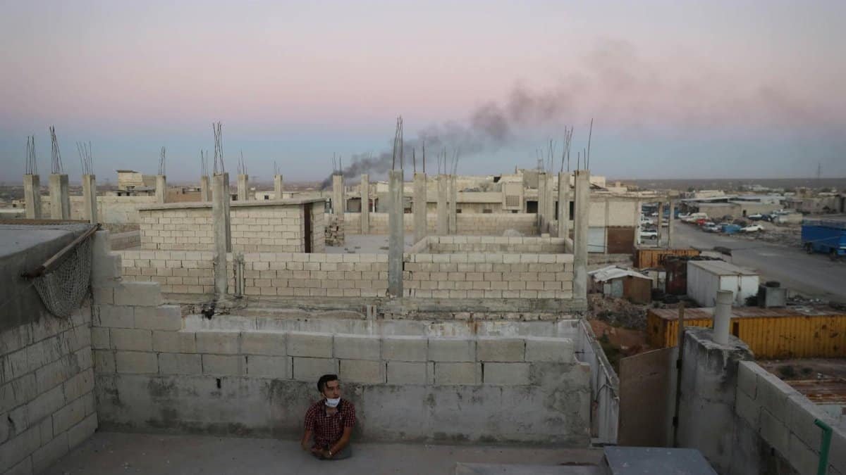 A lone man sits amid unfinished buildings in Syria during twilight, highlighting urban resilience.