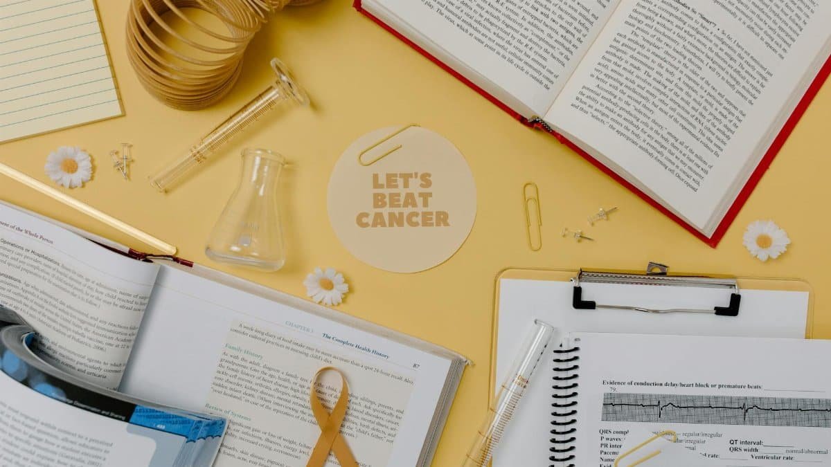 Flat lay of a research desk with open books, lab equipment, and a 'Let's Beat Cancer' card promoting cancer awareness.