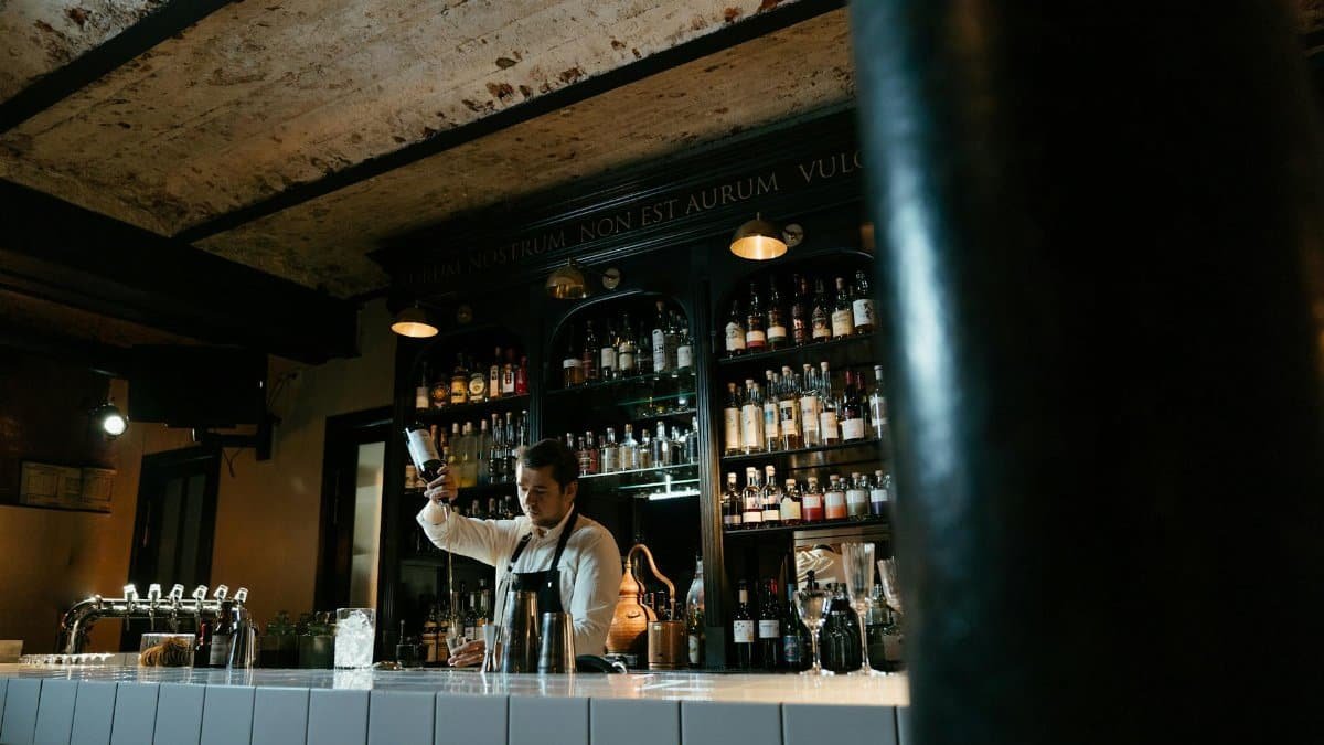 A bartender in uniform skillfully mixing a cocktail at a chic bar with various spirits displayed behind.